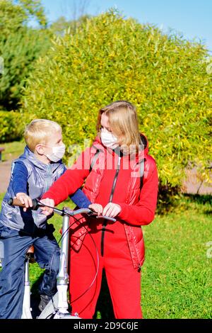 Mutter und Sohn im Vordergrund im Herbstpark in einer medizinischen Maske. Eltern lehren ihre Kinder. Stockfoto