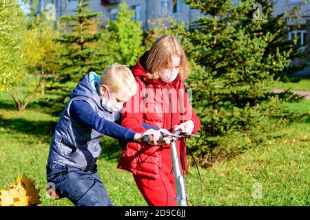 Mutter und Sohn im Vordergrund im Herbstpark in einer medizinischen Maske. Eltern lehren ihre Kinder. Stockfoto