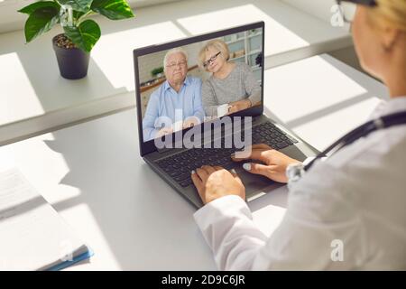 Gesichtsloser Arzt, der in ihrem Büro sitzt und mit einem älteren Paar per Videoanruf mit einem Laptop spricht. Stockfoto