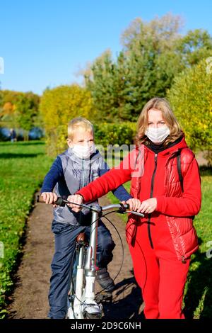 Mutter und Sohn im Vordergrund im Herbstpark in einer medizinischen Maske. Eltern lehren ihre Kinder. Stockfoto