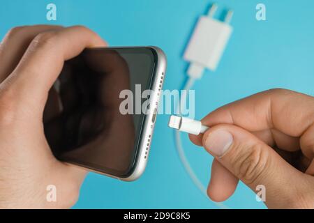 Nahaufnahme mans Hand Einstecken eines Ladegeräts in das Mobiltelefon über ein Lightning USB A Kabel. Stockfoto