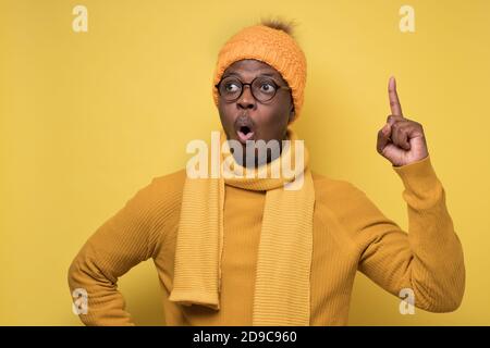 Afrikanischer Mann trägt warmen Schal und Hut zeigt Zeigefinger nach oben, mit Idee. Stockfoto