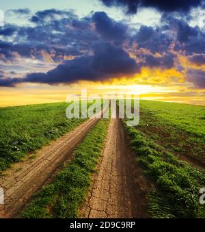 Ländlicher Weg bergauf Weg zu einem dramatischen Himmel am Sonnenuntergang über einem Grasfeld Stockfoto