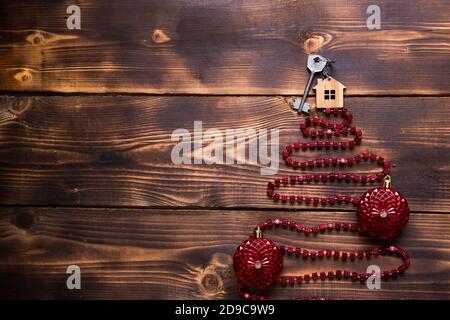 Schlüssel zum Haus mit einem Schlüsselanhänger auf dem Weihnachtsbaum aus roten quadratischen Perlen. Flach auf Holzhintergrund legen. Gebäude oder Kauf eines Hauses in New y Stockfoto