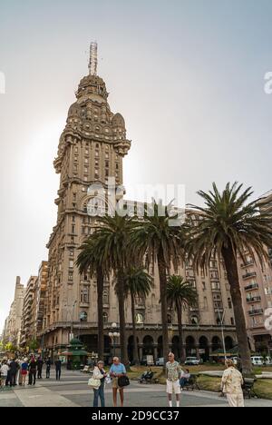 Montevideo, Uruguay- 18. Dezember 2008: Beigefarbener Stein ikonischen Palacio Salvo mit seinem einzigartigen Turm gegen silbernen Himmel. Unabhängigkeitsquadrat mit grünem Foli Stockfoto