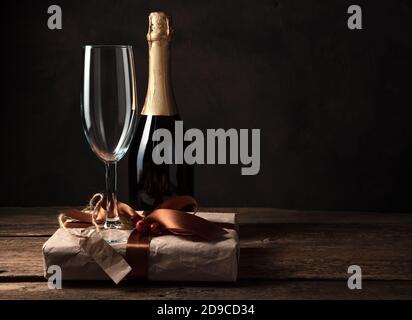 Geschenkbox, Champagner und Weinglas auf dunklem Holzhintergrund. Stockfoto