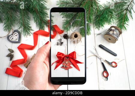 Telefon in der Hand einer Frau über einen Tisch mit Weihnachtsschmuck. Stockfoto