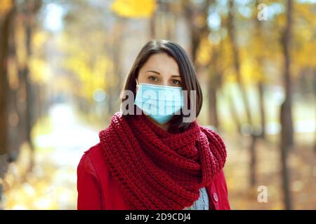 Schöne Frau in medizinischen Schutz Gesichtsmaske zu Fuß im Freien im Herbst Park. Coronavirus soziale Distanz Konzept. Stockfoto