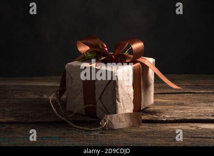 Geschenk eingewickelt in beigefarbenem Papier mit einem braunen Band auf einem dunklen Holzhintergrund. Stockfoto