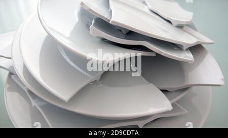 Haufen zerbrochener weißer Teller auf einem Glastisch Stockfoto