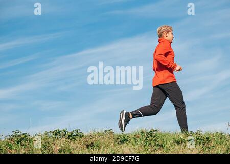 Mann in roten Langarm-Shirt, schwarze Laufhose und Schuhe laufen an der Straße mit blauen Himmel Hintergrund gekleidet Stockfoto