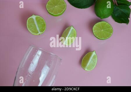 Zutaten für Mojito auf rosa Hintergrund. Leeres Glas, Stroh, Minze, Limette, Eiswürfel. Limette und Minze fallen in einen Cocktail spritzt Stockfoto