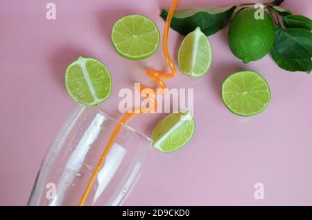 Zutaten für Mojito auf rosa Hintergrund. Leeres Glas, Stroh, Minze, Limette, Eiswürfel. Limette und Minze fallen in einen Cocktail spritzt Stockfoto