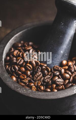 Geröstete Kaffeebohnen in Mörtel auf schwarzem Tisch. Stockfoto