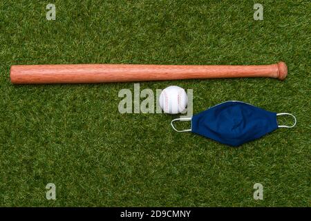 Baseballschläger, Ball und Maske isoliert auf einem Grasfeld. Baseball-Saison mit Gesichtsmaske. Sicheres Sportkonzept Stockfoto