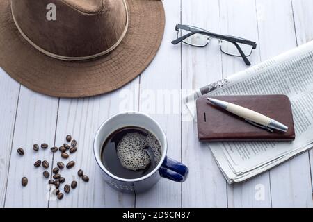 Ein Blick von oben auf eine Tasse Kaffee und Accessoires wie Hut, Brille, Stift, Zeitung und Handy. Stockfoto
