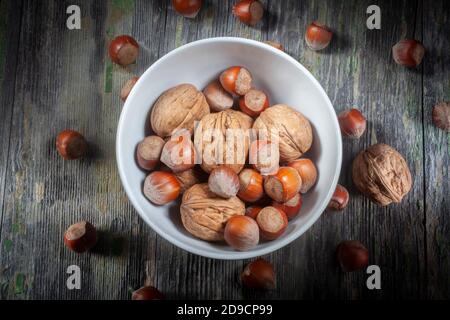 Bündel getrocknete Walnüsse und Haselnüsse in einer Keramikschale Auf verfallener Holzhintergrund Stockfoto