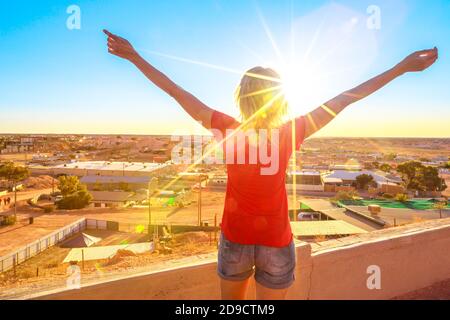 Unbeschwerte Frau, die mit offenen Armen vom Höhlenausblick aus den Panoramablick auf Coober Pedy bei Sonnenuntergang und die umliegende Wüste betrachtet. Südaustralisches Outback Stockfoto