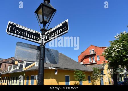 Ein traditioneller Straßenschild mit einer Lampe auf der Spitze weist den Weg zur Ursulines Street und Chartres Street im historischen French Quarter, New Orleans. Stockfoto