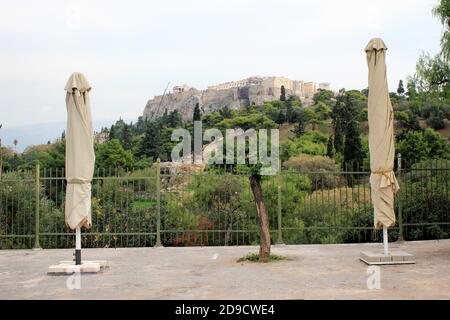 Griechenland, Athen, 3. November 2020 - geschlossene Schirme des leeren Cafe-Restaurants mit Akropolis-Hügel im Hintergrund, nach der Ankündigung für Covid-19 Stockfoto