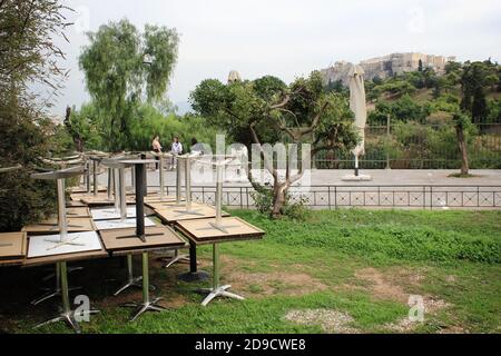 Griechenland, Athen, 3. November 2020 - Tische gestapelt vor geschlossenem Cafe-Restaurant mit Akropolis-Hügel im Hintergrund, nach der Ankündigung für Covi Stockfoto