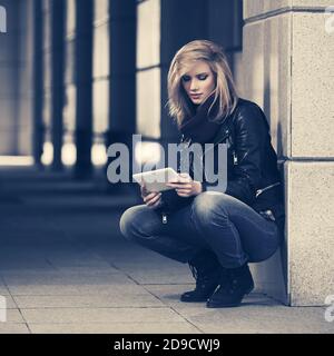 Junge Mode Frau mit digitalen Tablet auf City Street stilvoll Damenmodell in schwarzer Lederjacke und dunkelblauer Jeans Stockfoto