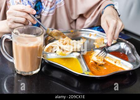 Person essen Roti prata oder Canai mit Curry und Dhal Stockfoto