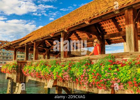 Blonde Frau in Rot auf der blumigen Brücke der Stadt Luzern, Reuss in der Schweiz. Chapel Bridge: Historische überdachte hölzerne Fußgängerbrücke, die Stockfoto