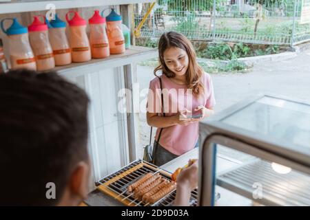 Frau wartet auf gegrilltes Wurstfutter, das gerade zubereitet wird Durch den Mann Stockfoto