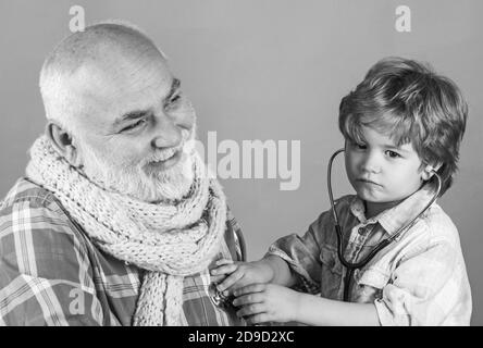 Glücklicher kleiner Junge im Arzt Kostüm mit Stethoskop auf farbigem Hintergrund. Kind spielen Arzt mit Papa auf farbigem Hintergrund. Stockfoto