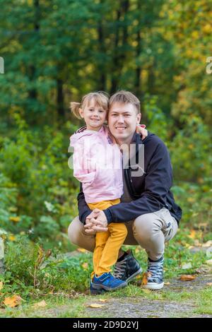 Ein Mädchen mit einem gebrochenen Arm umarmt ihren Vater Ein alter Park auf einem Herbstspaziergang Stockfoto