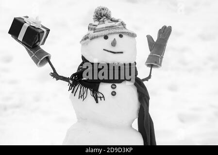 Niedlichen Schneemann in Hut und Schal auf schneebedeckten Feld mit Überraschung Weihnachtsgeschenk. Schneemann mit Einkaufstasche - Geschenkeinkaufkonzept. Glücklicher lächelnder Schneemann - Stockfoto