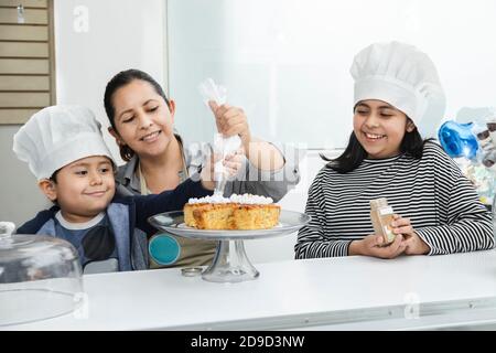Latina Mutter dekorieren einen Kuchen mit ihren Kindern - hispanisch Kinder haben Spaß in der Küche mit ihrer Mutter - Gebäck Kinder Stockfoto