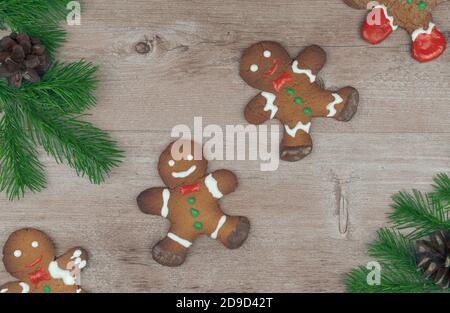 Lebkuchenmänner auf einer Holzoberfläche mit Fichtenzweigen verziert. Traditionelle Weihnachten Lebkuchenkekse. Urlaub Leckereien handgefertigt. Stockfoto