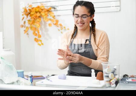 Hispanische Frau lächelt während der Arbeit in ihrem Konditorei - Junge Frau arbeitet mit Fondant, um einen Kuchen zu dekorieren - Junger lateinischer Unternehmer Konditor Stockfoto