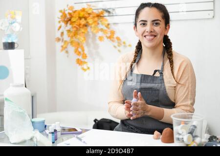 Hispanische Frau lächelt während der Arbeit in ihrem Konditorei - Junge Frau arbeitet mit Fondant, um einen Kuchen zu dekorieren - Junger lateinischer Unternehmer Konditor Stockfoto