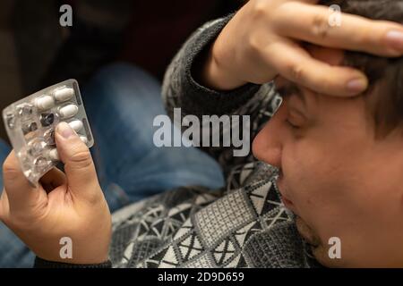 Eine Packung Pellets, Pillen in der Hand einer Person mit schlechter Gesundheit, die seine Hand über einen kranken Kopf hält Stockfoto