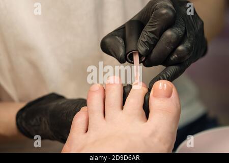 Pediküre. Gelpolieren. Durchscheinende Basisapplikation. Verarbeiten Pediküre aus nächster Nähe in einem modischen Spa-Salon, nicht erkennbare Menschen Stockfoto