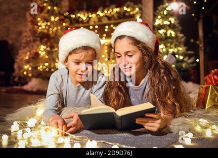 Kinder lesen zu Weihnachten ein Buch im Zimmer. Stockfoto