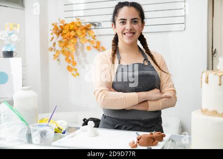 Junge lateinische Frau stolz in ihrer Konditorei - Frau Mit gekreuzten Armen und Blick auf die Kamera in ihrem Kuchen Workshop - unternehmungslustige hispanische Frau Stockfoto