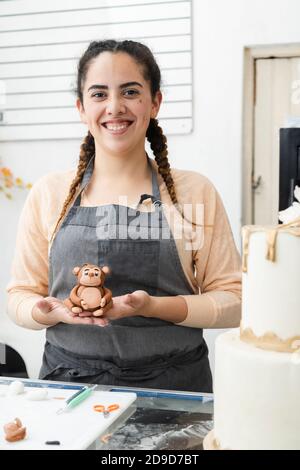 Junge lateinische Frau stolz in ihrer Konditorei - Frau Hält Fondant oder Ton Skulptur beobachten die Kamera in ihr Kuchenwerkstatt - unternehmungslustige hispanische Stockfoto
