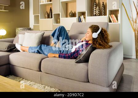 Junge Frau entspannt Musik zu Hause hören auf liegend Ein bequemes Sofa im Wohnzimmer mit einem Lächeln Des Vergnügens Stockfoto