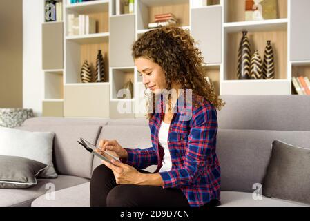 Ziemlich trendige junge Frau mit einem Tablet zu Hause durchsuchen Sie das Internet oder stellen Sie eine Verbindung zu sozialen Medien in einem her Nahaufnahme der Seitenansicht Stockfoto