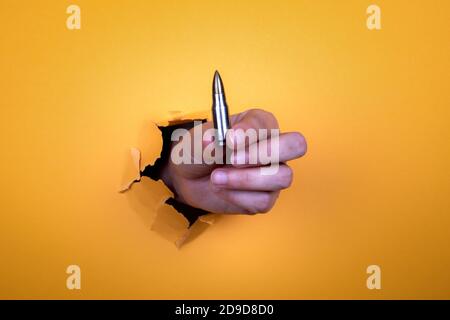 Kugel in Frauenhand. Einsatz von Schusswaffen, Gesetz und Ordnungskonzept. Orangefarbener Papierhintergrund Stockfoto