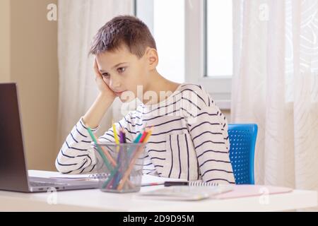 Trauriger, müder Junge, der zu Hause mit Büchern und einem Laptop am Tisch sitzt. Lernschwierigkeiten, Online-Bildungskonzept Stockfoto