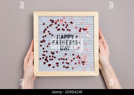 Hände halten Briefbogen mit Zitat Happy Vatertag auf grauem Hintergrund. Urlaubskonzept mit roten Sternen Konfetti. Stockfoto
