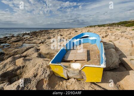 Gelbes Holzboot gestrandet auf steinigen Ufer mit dramatischen bewölkten Himmel nach Sturm. Menorca, Spanien Stockfoto