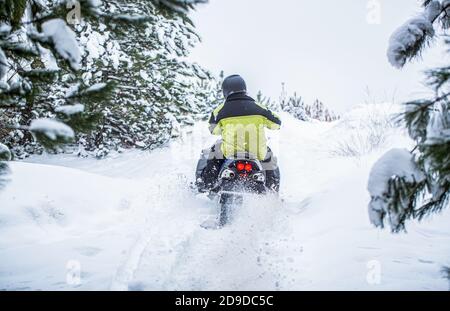 Der Mensch fährt Schneemobil in den Bergen. Pilot auf einem Sportschneemobil in einem Bergwald. Sportler fährt ein Schneemobil in den Bergen. Schneemobil in Stockfoto