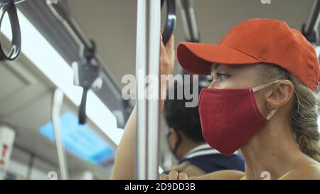 Frau fährt kaukasische Fahrt im überirdischen Zug airtrain mit Schutzmaske. Mädchen Tourist im airtrain mit Atemschutzmaske. Personenmaske. Stockfoto