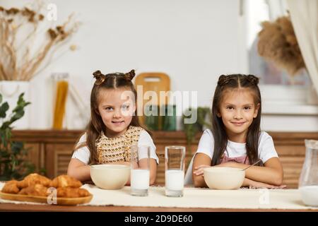 Glückliche kleine Freundinnen beim Frühstück - frische leckere Croissants und Milch in der Küche. Stockfoto